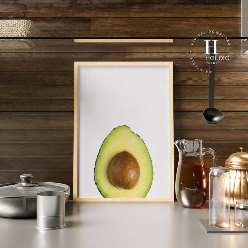 May include: A framed print of a halved avocado with a white background. The avocado is green with a brown pit.