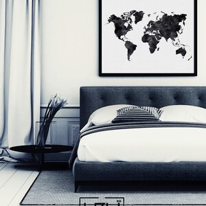 Puede incluir: Una impresi&oacute;n de mapa del mundo en acuarela en blanco y negro en un marco negro que cuelga sobre una cama tapizada en gris con ropa de cama blanca y una almohada a rayas en blanco y negro.