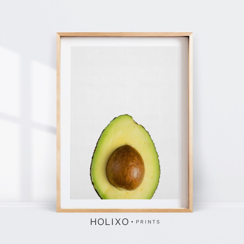 May include: A framed print of a halved avocado with a brown pit on a white background. The frame is light wood.