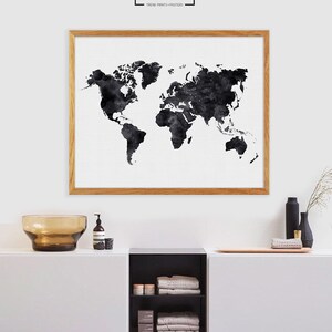Puede incluir: Una impresi&oacute;n de mapa del mundo en acuarela en blanco y negro en un marco de madera, colgada en una pared blanca sobre un armario blanco con un estante negro y toallas marrones.
