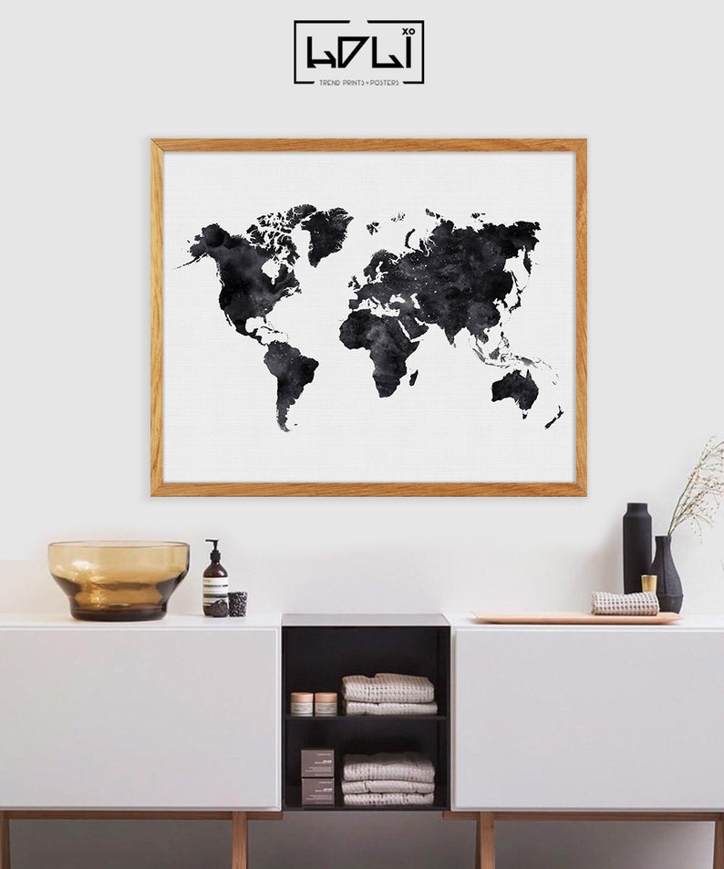 Puede incluir: Una impresi&oacute;n de mapa del mundo en acuarela en blanco y negro en un marco de madera, colgada en una pared blanca sobre un armario blanco con un estante negro y toallas marrones.