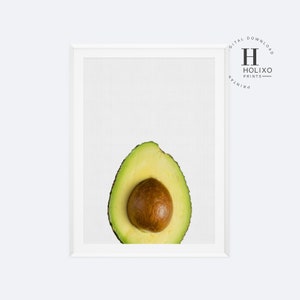May include: A close-up of a halved avocado with the pit still inside. The avocado is green and the pit is brown. The avocado is on a white background.