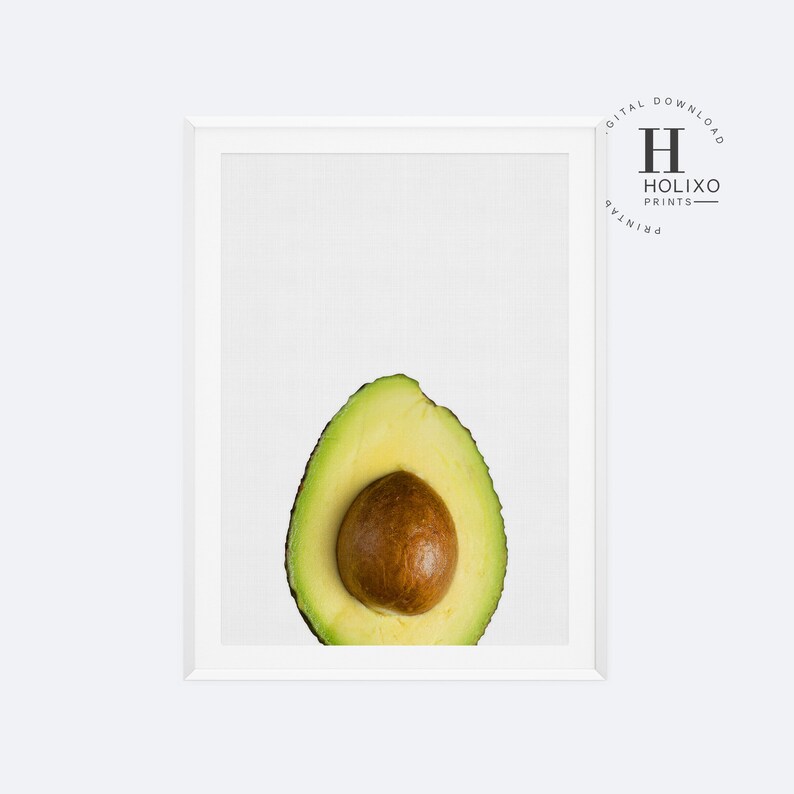 May include: A close-up of a halved avocado with the pit still inside. The avocado is green and the pit is brown. The avocado is on a white background.
