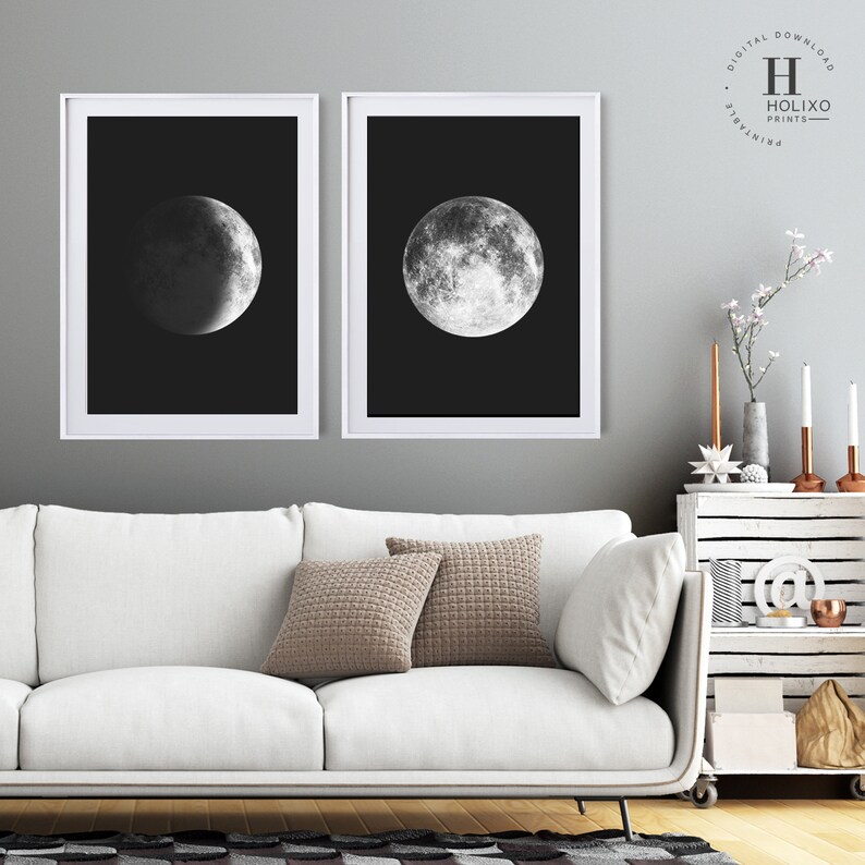 May include: Two black and white framed prints of the moon in different phases. The prints are hanging on a gray wall above a white couch with two brown throw pillows.