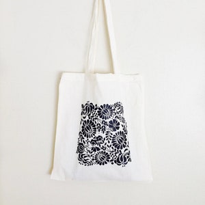 May include: A white canvas tote bag with black floral pattern printed on the front.