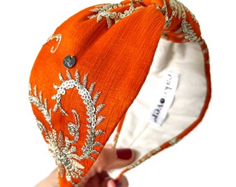 May include: Orange fabric headband with a silver floral design and a small tag that says "Cal.o.ver".
