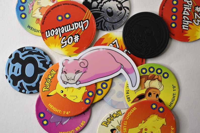 Puede incluir: Una colecci&oacute;n de cartas de intercambio de Pok&eacute;mon coloridas con varios personajes, incluyendo Charmeleon, Pikachu y Eevee. Las cartas son circulares y tienen un dise&ntilde;o en blanco y negro con el nombre y el n&uacute;mero del Pok&eacute;mon impresos en ellas. Las cartas est&aacute;n dispuestas en un orden aleatorio sobre una superficie blanca.