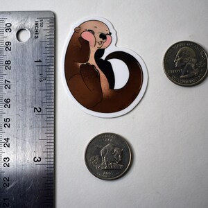 May include: A brown and white cartoon otter sticker with pink cheeks, smiling and holding its paws together. The sticker is about the size of a US quarter.