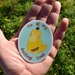 May include: An oval sticker featuring a yellow cartoon duck with a sad expression and a knife. The duck is on a light blue background with the words "I'm at my ducking limit" in a circular layout.
