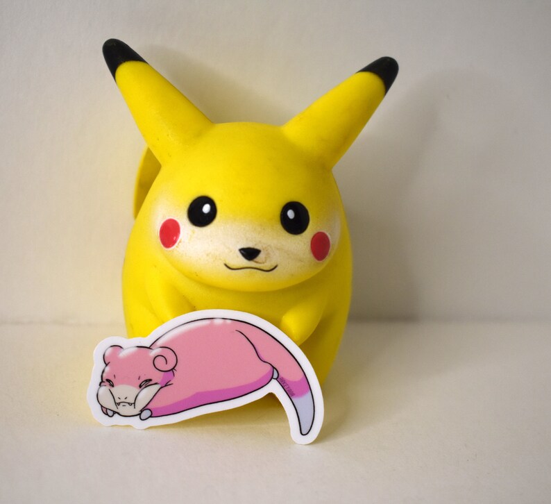 Puede incluir: Una figura de Pikachu amarilla con ojos negros y mejillas rojas. Una pegatina rosa y blanca de un personaje de dibujos animados est&aacute; delante de la figura.