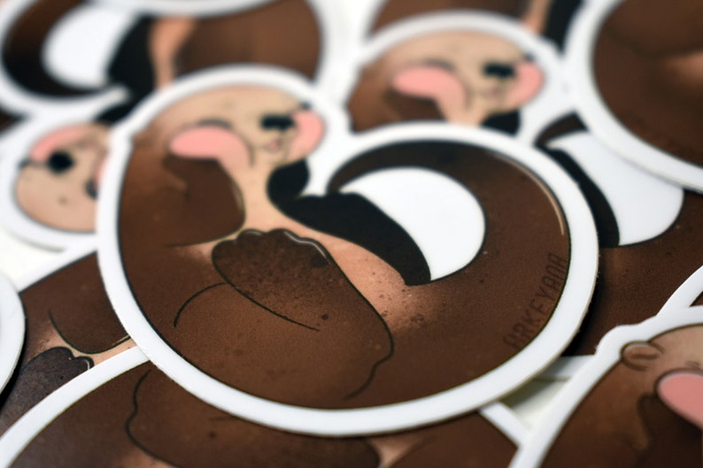 May include: Close-up of a stack of brown and white round stickers featuring a cartoon otter with a curled tail. The otter is brown with a white belly and a pink nose. The text "ORKEYBOO" is printed on the sticker.