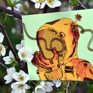 Könnte beinhalten: Ein quadratischer Aufkleber mit hellgrünem Hintergrund zeigt eine Illustration einer Person in einem gelben Kapuzenkleidungsstück mit einem Netzgesichtsschutz. Die Illustration ist in Orange- und Brauntönen gehalten, mit dem Text "HELLO SHROOMS" sichtbar. Eine Blume und Linien erstrecken sich von der Figur.