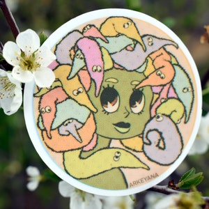 May include: A round sticker with a cartoon illustration of a green-skinned person with large eyes and a pink mouth surrounded by colorful worms. The text "ARKEYANA" is at the bottom of the sticker.