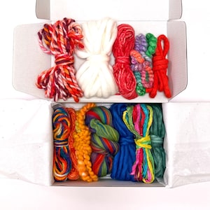 May include: A white cardboard box containing an assortment of yarn bundles in various textures and colors, including variegated red, white, solid red, green, orange, blue, and multi-colored strands arranged in two horizontal rows within the box.