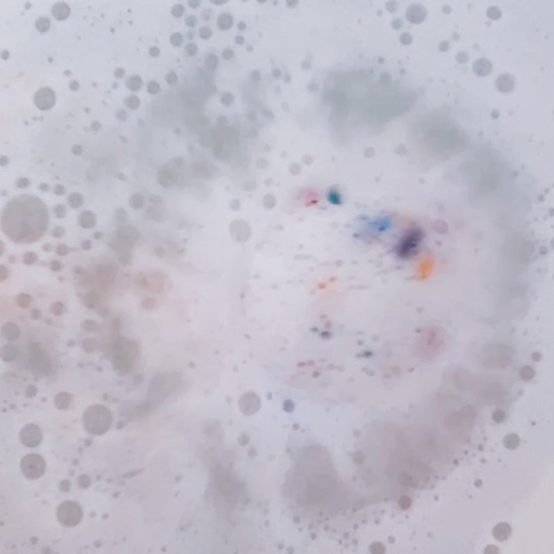 May include: Close-up of a bath with white bubbles and colorful specks. The bubbles vary in size, creating a textured surface. The colorful specks include shades of blue, purple, orange, and pink, adding visual interest to the bath water.