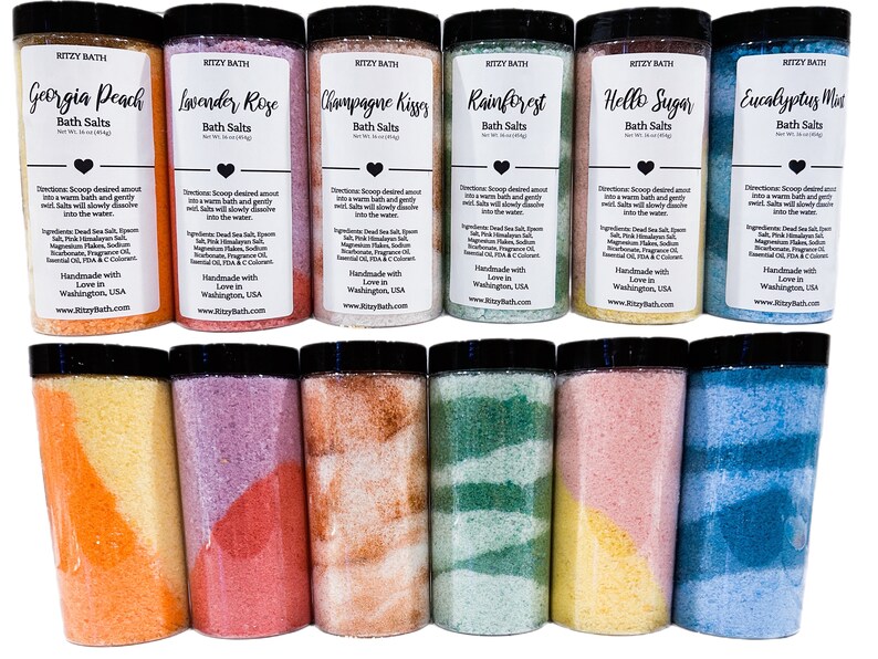 May include: Eight clear jars of bath salts with colourful layers. The jars are labelled with different scents, including Georgia Peach, Lavender Rose, Champagne Kisses, Rainforest, Hello Sugar, and Eucalyptus Mint. Each jar has a black lid.