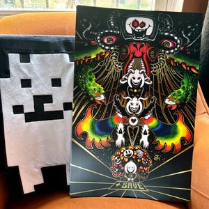 May include: A pixelated black and white plush toy and a poster with a detailed, colourful illustration. The poster features a central figure with multiple eyes and a complex design, with the word "SAVE" at the bottom.