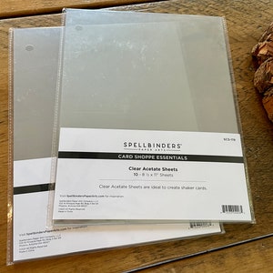 May include: A package of 10 clear acetate sheets, 8 1/2 by 11 inches, for creating shaker cards. The package is labeled "Spellbinders Paper Arts Card Shoppe Essentials Clear Acetate Sheets".
