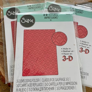 May include: Several Sizzix 3-D textured impressions embossing folders in clear plastic packaging. The folders are A5 size and feature a repeating geometric pattern in a reddish-pink color. The packaging includes the Sizzix logo and multilingual text.
