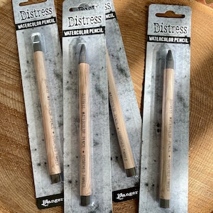 May include: Three packages of Distress Watercolor Pencils in the color Scorched Timber. Each package has a black and white image of a pencil with the text "Distress Watercolor Pencil" and "Scorched Timber" printed on the package.