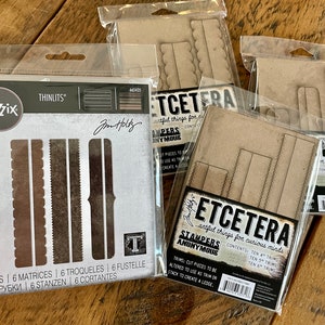 Puede incluir: Un juego de seis troqueles de metal para manualidades. Los troqueles tienen forma de diferentes bordes y marcos. Los troqueles están empaquetados en una bolsa de plástico transparente con fondo blanco y texto negro. El texto del paquete dice "Sizzix Thinlits" y "Jim Holtz".