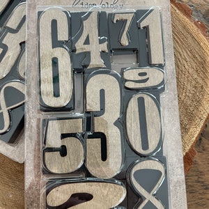 May include: A package of ten wooden number blocks. The numbers are in a light brown color with a dark gray border. The package has the text "NUMBER BLOCKS" and "10 PIECES".
