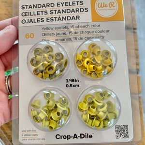 May include: A package of 60 yellow standard eyelets, 15 of each color. The eyelets are 3/16 inch (0.5 cm) in size and are packaged in clear plastic containers. The package is labeled "We R memory keepers" and "Crop-A-Dile".