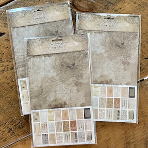 May include: Three packages of patterned paper for scrapbooking or crafting. Each package features a different design with a vintage aesthetic. The paper is double-sided and includes a variety of patterns and textures. The packages are labeled "Jim Holtz Idea-ology" and "Volume 14 Time Flies".