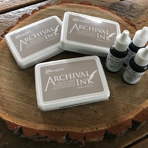 May include: Three ink pads and three bottles of archival ink in the color Pebble Beach. The ink pads and bottles are all labeled with the Ranger brand name.