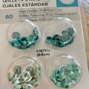 May include: A package of 60 standard eyelets in aqua and turquoise colors. The eyelets are 0.1875 inches (0.5 cm) in diameter. The package is labeled "We R memory keepers".