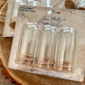 May include: A package of three clear glass display domes with cork stoppers. The package is labeled "Jim Holtz ide-ology" and "Display Domes/Dome d'Affichages". The domes are labeled "Mini/Mini".