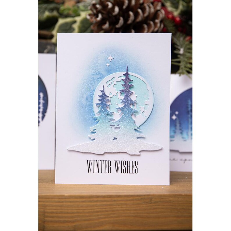 May include: A white card with a blue and white winter scene with a full moon and two trees. The text "Winter Wishes" is printed at the bottom of the card.