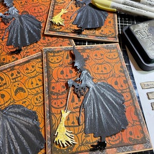 May include: Halloween-themed greeting cards featuring a black witch silhouette holding a broom. The cards have an orange background with pumpkin faces and a brown border. The witch's dress and hat are black, and the broom is yellow.