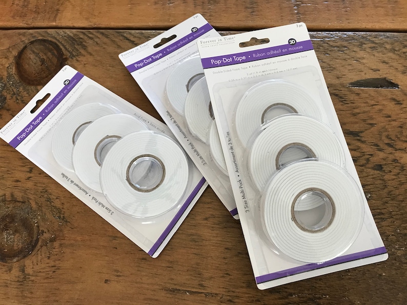 May include: Three packs of white Pop-Dot Tape, each pack containing three rolls of tape in different sizes. The tape is double-sided and adhesive, and is designed for mounting and securing items without damaging surfaces.