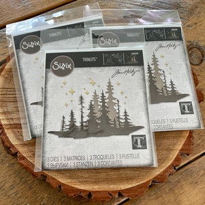 May include: Three die-cut metal stencils for crafting, featuring a forest scene with trees and stars. The stencils are packaged in clear plastic bags and labeled "Sizzix Thinlits" with the product number "664334".