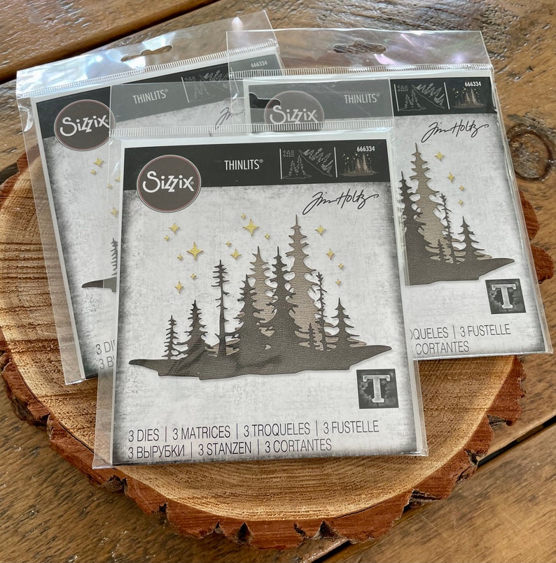 May include: Three die-cut metal stencils for crafting, featuring a forest scene with trees and stars. The stencils are packaged in clear plastic bags and labeled "Sizzix Thinlits" with the product number "664334".