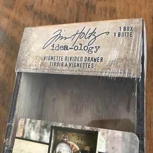May include: A wooden box with a clear plastic window showing a divided drawer with compartments for organizing small items. The box is labeled "Jim Holtz idea-ology Vignette Divided Drawer Tiroir à Vignettes 1 Box 1 Botte".