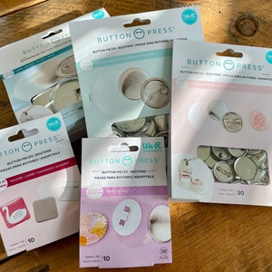 May include: Assortment of We R Makers Button Press kits for making buttons. The kits include different sizes and shapes of buttons, including square, oval, and round. The kits also include the necessary tools and instructions for making buttons.
