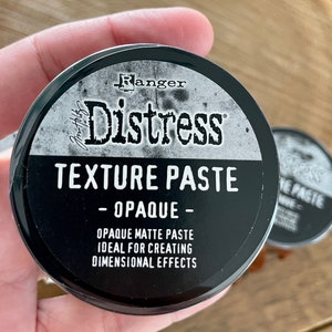 May include: A black jar of Ranger Distress Texture Paste, labeled "Opaque Matte Paste, Ideal for Creating Dimensional Effects".