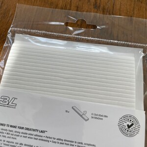 May include: A package of 76 white double-sided adhesive foam strips. The package is labeled "3L Consumer Products A/S" and "Designed to make your creativity last". The strips are 0.12 inches by 3.93 inches by 0.08 inches, or 3 mm by 100 mm by 2 mm.