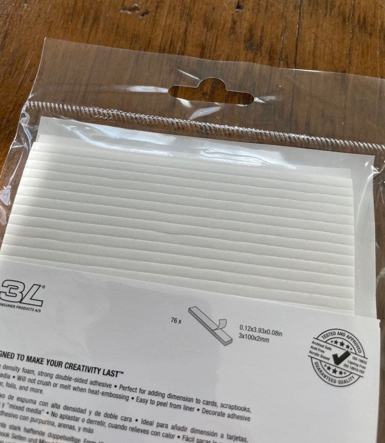 May include: A package of 76 white double-sided adhesive foam strips. The package is labeled "3L Consumer Products A/S" and "Designed to make your creativity last". The strips are 0.12 inches by 3.93 inches by 0.08 inches, or 3 mm by 100 mm by 2 mm.