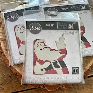May include: Several packages of Sizzix Thinlits dies featuring a Santa Claus design. The Santa die cuts are red, cream, and black. The packaging includes the text "Jim Holtz" and "6 Dies".