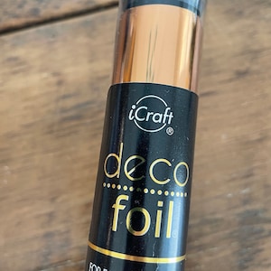 May include: A roll of gold deco foil for crafting. The label reads "iCraft deco foil" and "For fabric and paper, Pour le tissu et le papier, Para la tela y papel".
