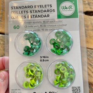 May include: Package of 60 green eyelets, 15 of each color, 3/16 inch (0.5 cm) in size. The eyelets are packaged in three clear plastic containers. The package is labeled "Standard Eyelets" and "We R memory keepers". The package also includes instructions for use with a Crop-A-Dile tool.