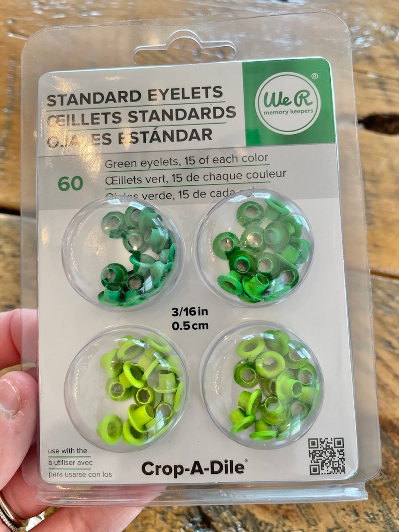 May include: Package of 60 green eyelets, 15 of each color, 3/16 inch (0.5 cm) in size. The eyelets are packaged in three clear plastic containers. The package is labeled "Standard Eyelets" and "We R memory keepers". The package also includes instructions for use with a Crop-A-Dile tool.