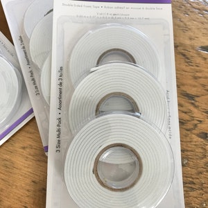 May include: A package of three rolls of double-sided foam tape. The tape is white and has a 3D pop-dot design. The package is labeled "Pop-Dot Tape" and "Ruban adh&eacute;sif en mousse".