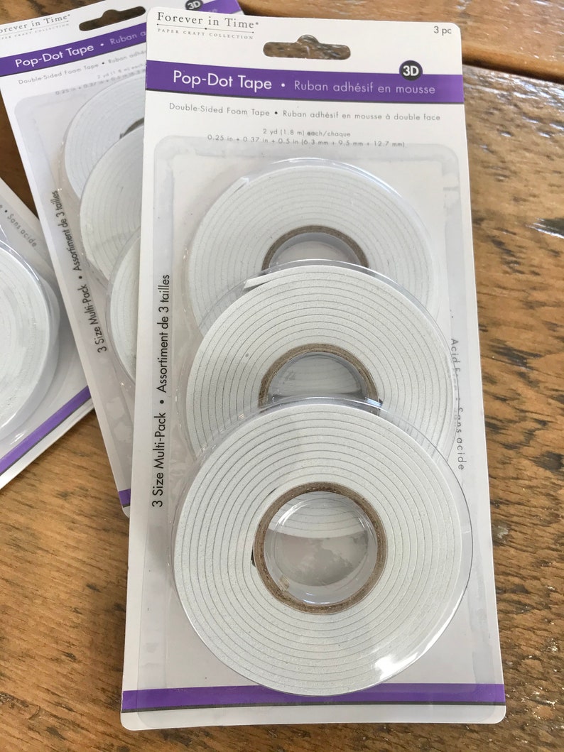 May include: A package of three rolls of double-sided foam tape. The tape is white and has a 3D pop-dot design. The package is labeled "Pop-Dot Tape" and "Ruban adh&eacute;sif en mousse".