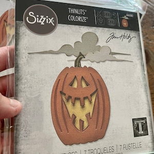 May include: A package of 7 Sizzix Thinlits Colorize dies featuring a pumpkin with a carved jack-o-lantern face. The package is labeled "Thinlits Colorize" and "Jim Holtz". The dies are designed for use with a die-cutting machine.
