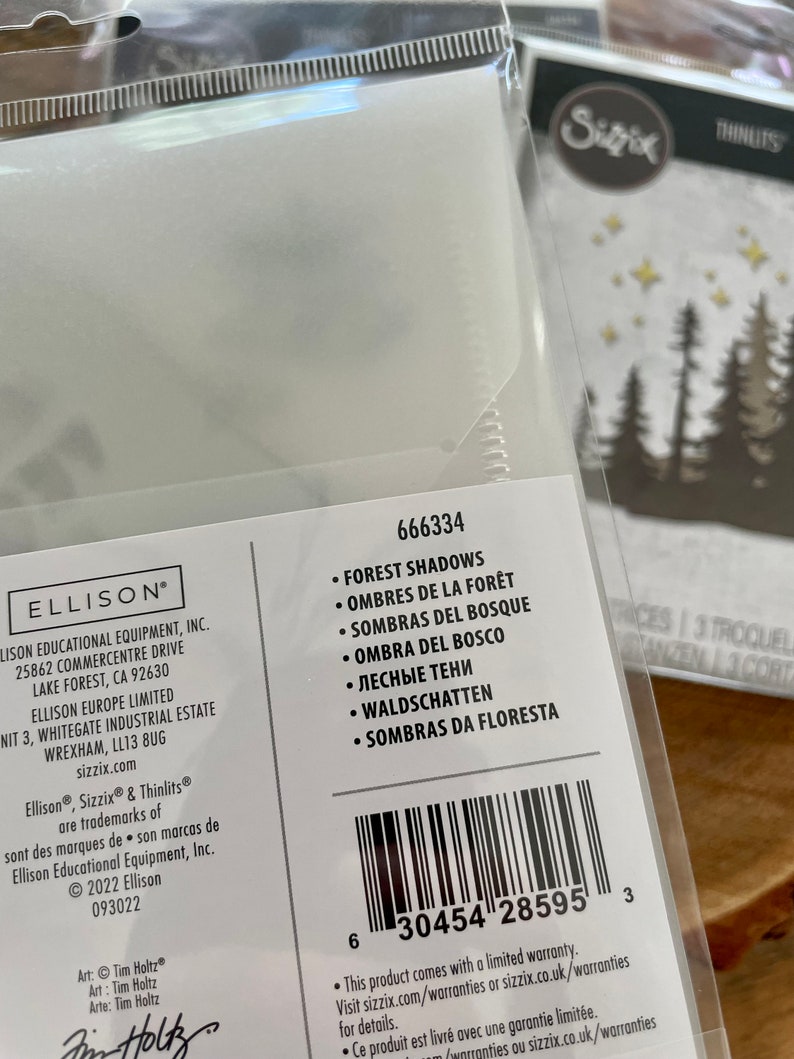 May include: A white package with a barcode and product information for a set of forest shadows dies. The package includes the product name, product number, and a list of languages for the product name. The product is made by Ellison Educational Equipment, Inc. and is part of the Sizzix brand.
