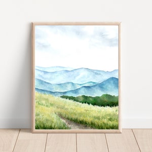 May include: Watercolor painting of a landscape with blue mountains and a green field with a dirt path leading through it.